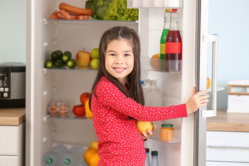 Little Asian girl choosing food from fridge in kitchen