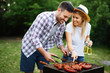 © NDABCREATIVITY - Young couple preparing sausages on a barbecue outdoors