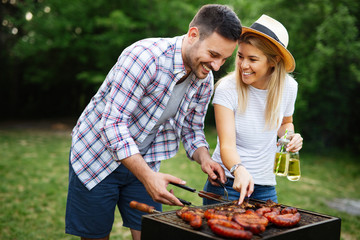 Wall Mural - Young couple preparing sausages on a barbecue outdoors