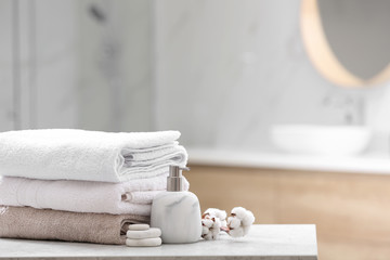 Clean towels, spa stones and soap dispenser on table in bathroom. Space for text