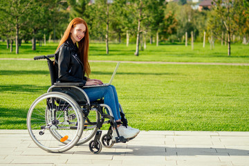 redhead ginger freelancer woman sitting in wheelchair and working by laptop in summer park