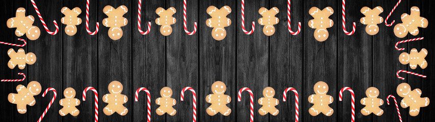 Gingerbread mea and candy canes isolated on black dark wooden rustic table - top view with space for text, background panorama banner long