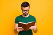 © deagreez - Portrait of focused college student guy hold read textbook learn information for study project wear spectacles good looking clothes isolated over yellow color background