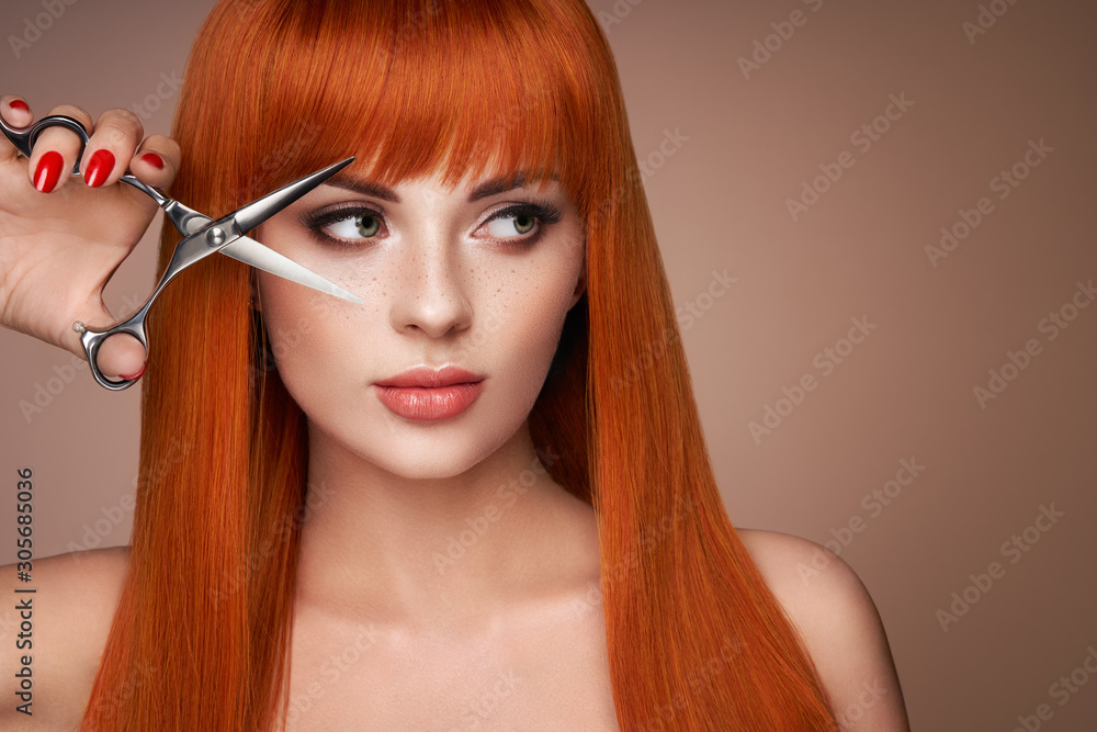 Beautiful young woman with a bright makeup and a smooth long hair holds metal scissors. Model with red hair. Hair salon, haircut. Care and beauty hair products. Perfect make-up - obrazy, fototapety, plakaty 