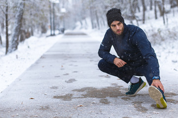 Young man stretching before running in city park at cold winter day.