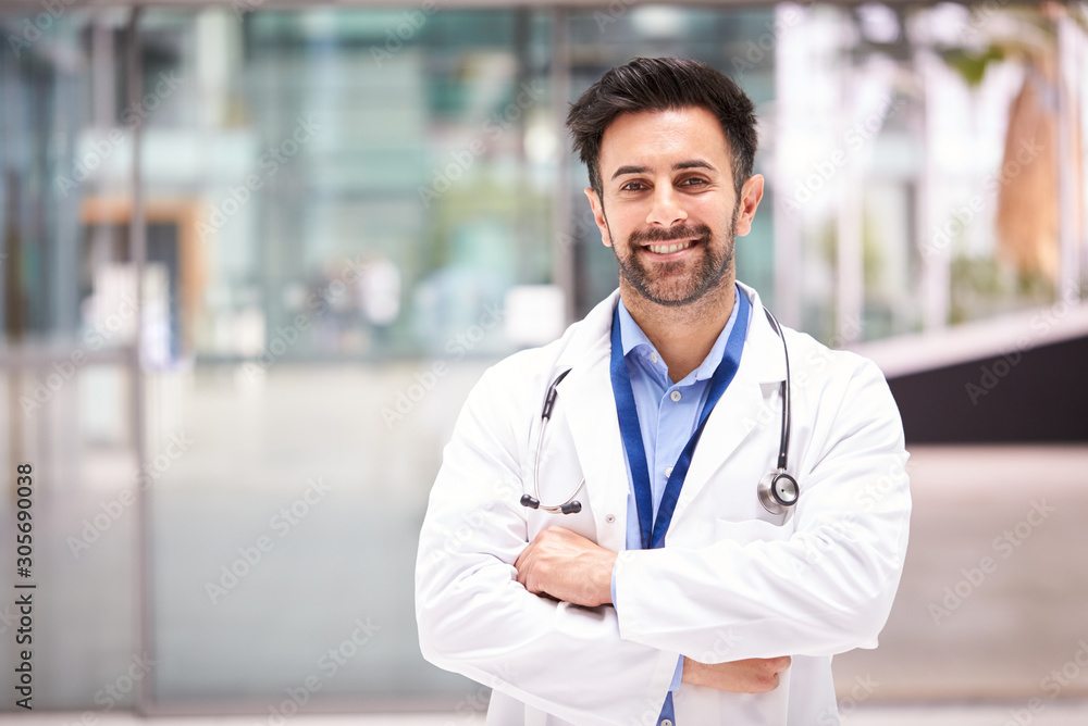 Portrait Of Male Doctor With Stethoscope Wearing White Coat Standing In Modern Hospital Building - obrazy, fototapety, plakaty 