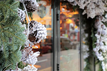 Christmas Decorations In A Shop Window On A City Street. Fir Branches And Pine Cones In Winter, New Year Celebration, Magic Of The Holiday
