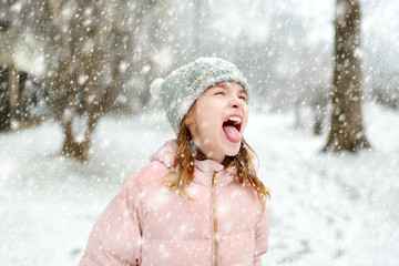 Adorable young girl catching snowflakes with her tongue in beautiful winter park. Cute child playing in a snow.