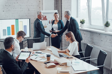 Canvas Print - Confident businessmen shaking hands and smiling while working together with colleagues in the board room