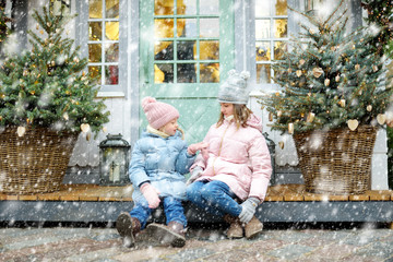 Two adorable sisters having a good time together on traditional Christmas fair in Riga, Latvia. Children enjoying sweets, candies and gingerbread on Xmas market.