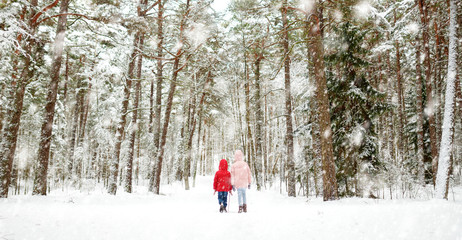 Two adorable little girls having fun together in beautiful winter forest. Beautiful sisters playing in a snow.