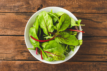 Overhead shot of green mixed salad with spinach, arugula and beetroot leaves in bowl on old wooden background