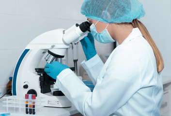 Young female scientist studying new substance or virus in microscope