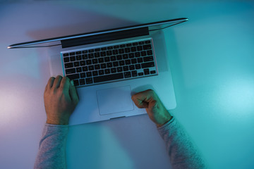 Aufkleber - Man working night online silver laptop in the color light on a table night background. Top view.