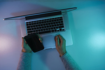 Aufkleber - Man working night online silver laptop and smart phone in the color light on a table night background. Top view.