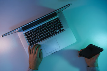 Aufkleber - Man working night online silver laptop and smart phone in the color light on a table night background. Top view.