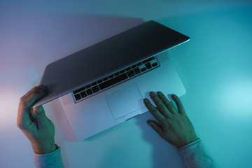 Aufkleber - Man open silver laptop night online in the color light on a table night background. Top view.