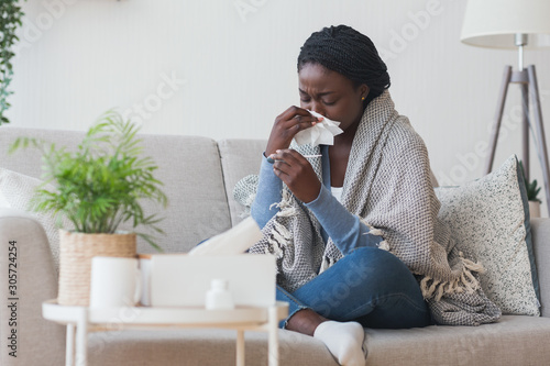 Cuadros en Lienzo Black girl having flu, blowing nose and checking body temperature