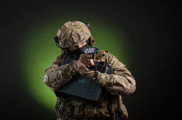 Wall Mural - a male soldier in military clothes with a weapon on a dark background