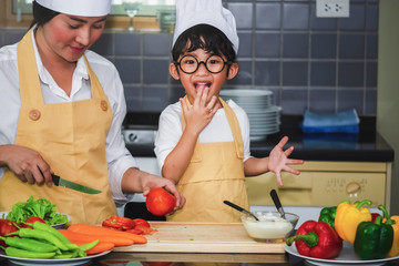 Wall Mural -  Asian woman young mother with son boy cooking salad mom sliced vegetables food son tasting salad dressing vegetable carrots and tomatoes bell peppers happy family cook lifestyle kitchen