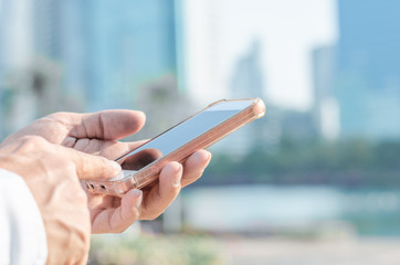 close up business man using hand typing smartphones and touch screen working search with app devices outdoor in city with sunrise and building background. 5G technology connecting the world.