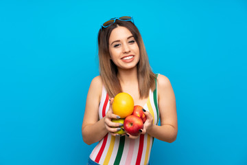Wall Mural - Young woman in summer holidays over blue background holding fruits