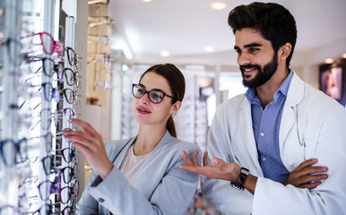 Wall Mural - Young woman in optic store choosing a new glasses. Medical, health care concept