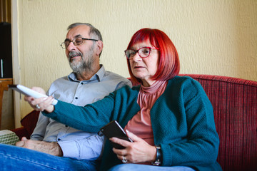 Front View Of A happy senCouple Watching Movie On Television At Home. Amazed senior couple watching tv program sitting on a couch at home. Advertising to Baby Boomers on TV