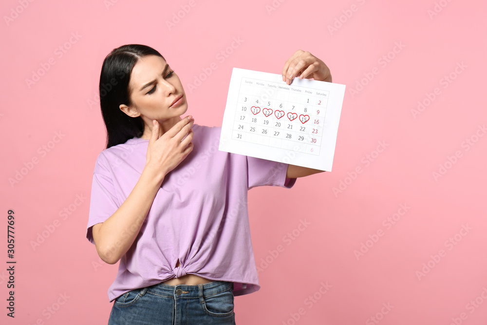 Pensive young woman holding calendar with marked menstrual cycle days on pink background - obrazy, fototapety, plakaty 