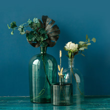 Various Artificial Flowers And Dry Plants In Transparent Vases On The Floor Against Blue Wall. Fine Art Flower Composition