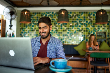 Handsome millennial indian man working in trendy coworking space