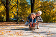 Happy smiling granddaughter enjoying day with grandmother in the autumn park while riding skateboard
