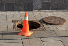 Open Sewer Manhole Cover And Traffic Cone On A City Street. Sewerage Repair. Emergency Service And Accident. Drainage System Maintenance. Danger Sign