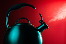Photo Of Stainless Steel Kettle In Neon Light Over Red Background. Steam From The Kettle Through The Whistle.