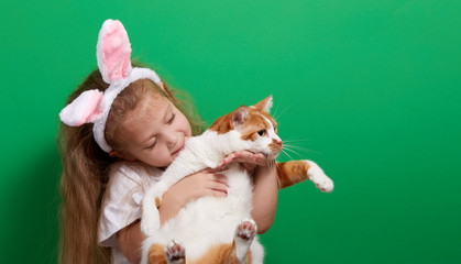 cute happy chikd girl with a real easter pet cat wearing ears on green background