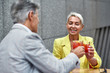 © Svitlana - Cheers. Cheerful and beautiful middle-aged woman in yellow suit jacket drinking cocktails with her friend and smiling while sitting in cafe outdoors together