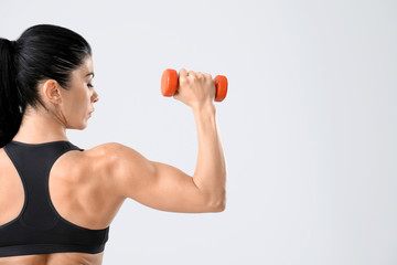 Sticker - Sporty muscular woman with dumbbell on light background