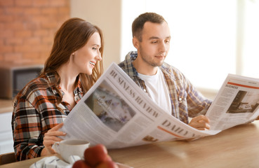 Canvas Print - Beautiful young couple reading newspapers in kitchen