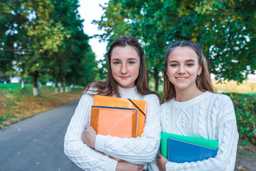 Two teenage girls teenagers, best girlfriends, summer city park, holding notebooks notes, emotions of happiness smiles fun. Free space for copy text. Concept of relaxation after school and college.