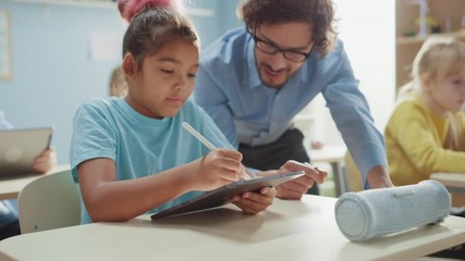 Wall Mural - Elementary School Computer Science Class: Cute Girl Uses Digital Tablet Computer, Friendly Teacher Helps Her with the assignment. Children Getting Modern Education in STEM, Playing and Learning