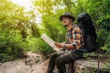 Man Traveler With Backpack Sitting And Reading Map In The Forest
