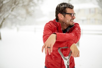 Wall Mural - Closeup shot of a male with his hands on the snow shovel and wearing a red jacket on a snowy day