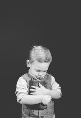 Wall Mural - Vertical grayscale shot of a child holding the bible with his eyes closed