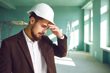 Builder foreman in a white helmet surprised in shock at a construction site indoors