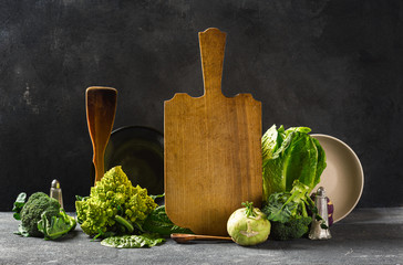 Still life kitchen board with fresh green vegetables on dark background. Cooking healthy food concept