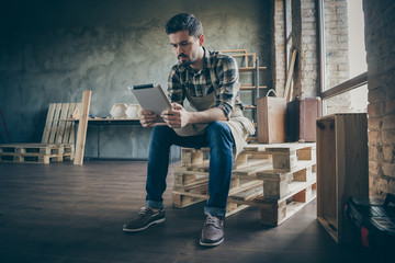 Photo of handsome guy holding e-book website administrator reading new orders checking email dinner time wooden business industry woodwork shop garage indoors