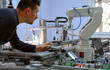 © Ridvan - industry 4.0 concept: A mechatronics engineer is holding product and teaching robot arm the positions with teach pendant on smart factory production line background. Selective Focus.