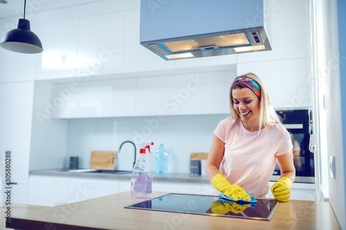 Cuadros en Lienzo Worthy cheerful caucasian blond housewife with rubber gloves on hands cleaning stove