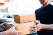© wutzkoh - Asian cargo carrier holds a cardboard box with the package inside and the recipient is signing the package.
