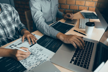 Two software developers are using computers to work together with their partner at the office desk.